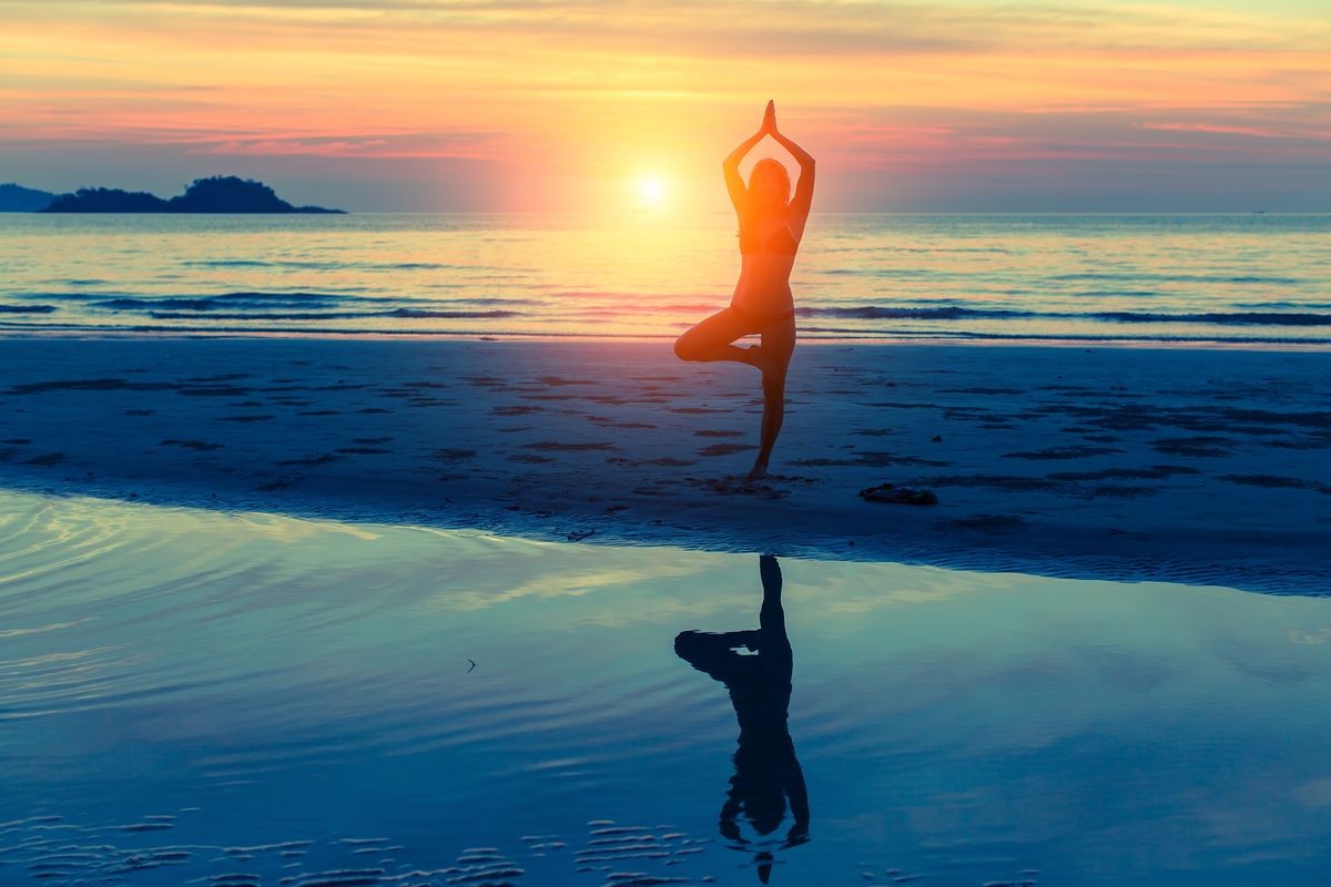 Young woman practicing yoga on the beach at sunset with reflection in water. Health and beauty.